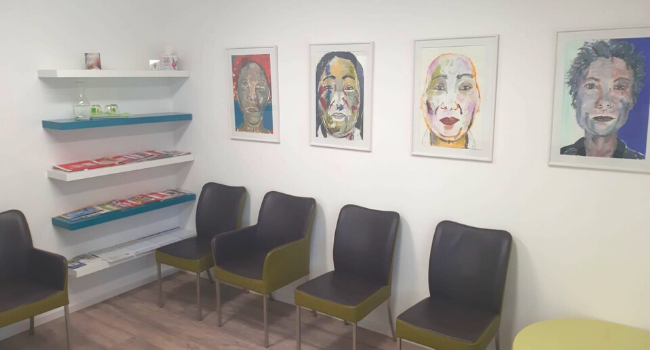 Wartezimmer mit künstlerischen Portraits und Magazinen in der Praxis von DentisBavaria