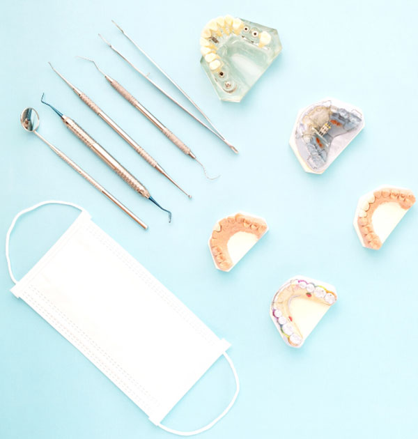 Zahnarztbesteck, Einwegmaske und diverse Kiefermodelle auf blauer Unterlage