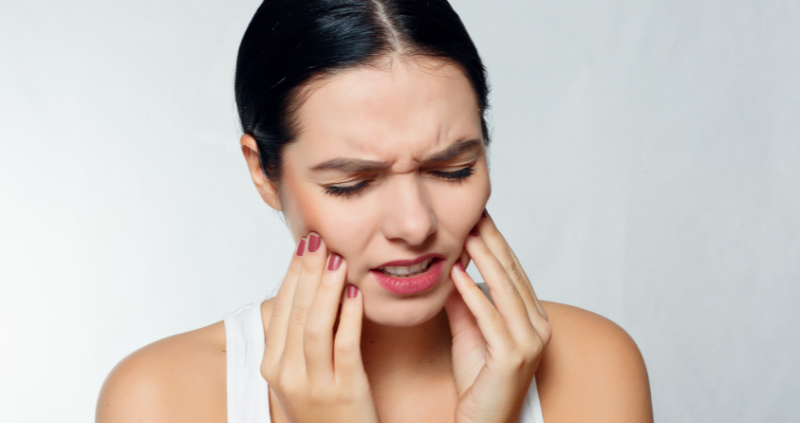 Frau mit schmerzempfindlichen Zähnen hält sich mit beiden Händen die Wangen.
